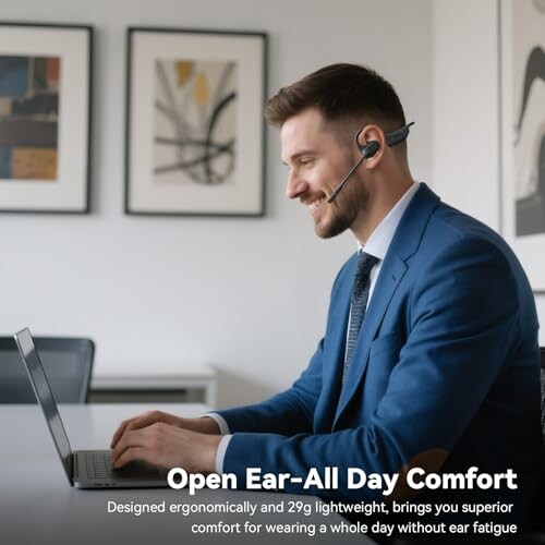 Man in blue suit using a laptop with a headset, sitting at a desk.