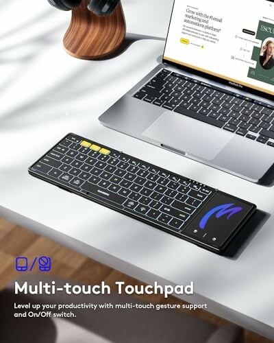 Keyboard with multi-touch touchpad on a desk beside a laptop.